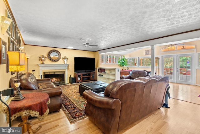 living room featuring a textured ceiling, crown molding, ceiling fan, a lit fireplace, and light wood-type flooring
