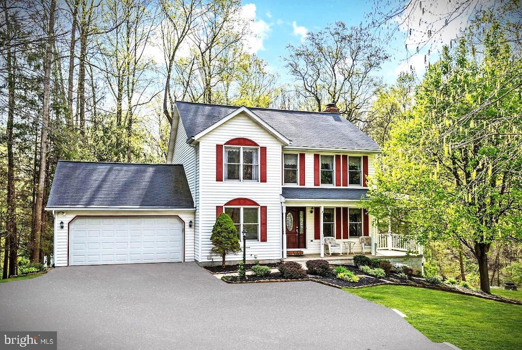 view of front of house featuring a front lawn, an attached garage, aphalt driveway, a chimney, and a porch