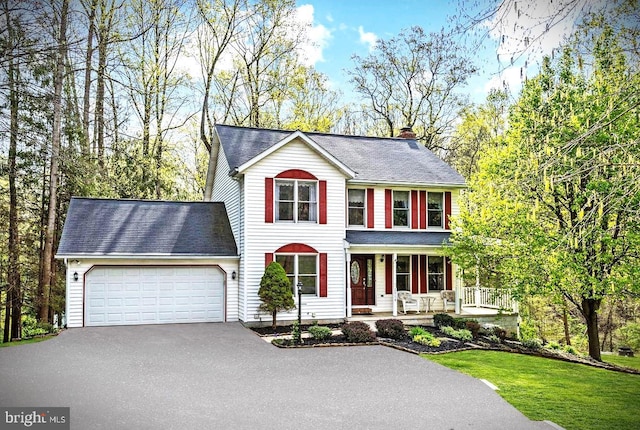 view of front of house featuring a front lawn, an attached garage, aphalt driveway, a chimney, and a porch
