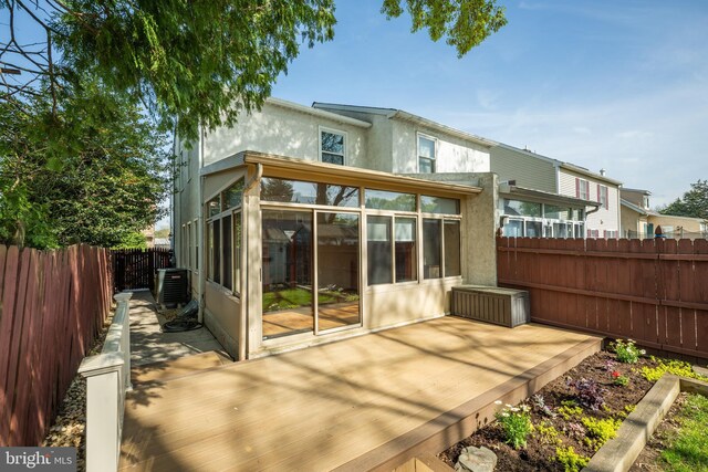 rear view of property with a wooden deck, central air condition unit, a sunroom, stucco siding, and a fenced backyard