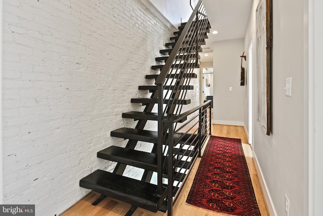 stairway with brick wall, baseboards, and wood finished floors