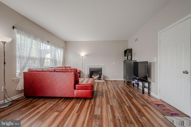 living area with baseboards, wood finished floors, visible vents, and a tiled fireplace