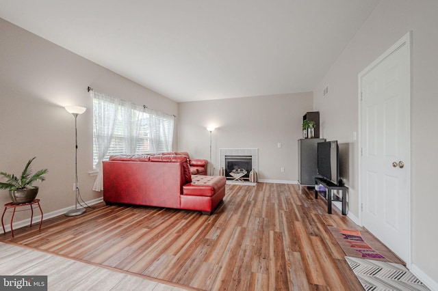 living room featuring visible vents, a tiled fireplace, light wood-style flooring, and baseboards