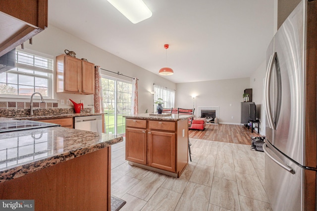 kitchen featuring stainless steel appliances, a sink, light stone countertops, a glass covered fireplace, and open floor plan