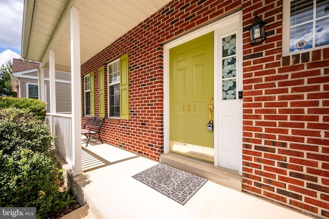 entrance to property featuring a porch and brick siding