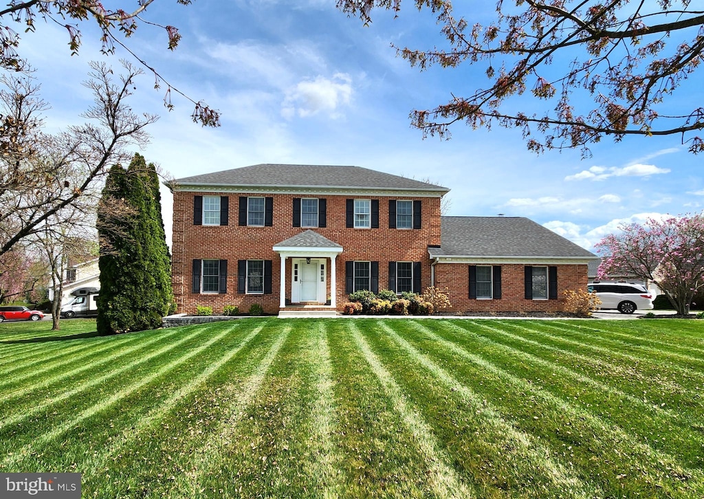 colonial house with brick siding, a shingled roof, and a front yard
