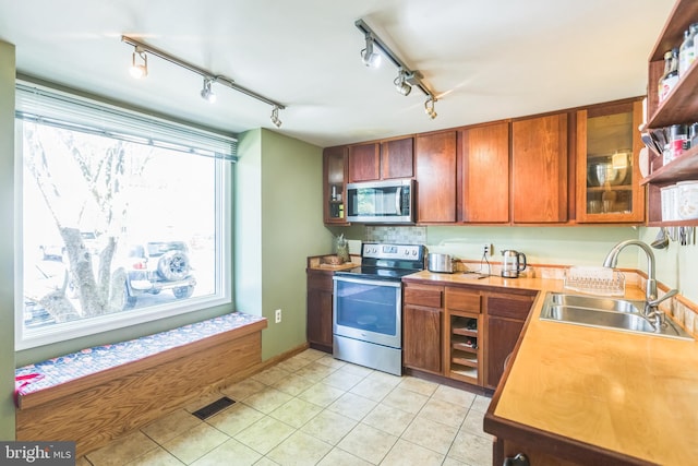 9427 Candleberry Ct, Burke, VA 22015 - kitchen featuring glass insert cabinets, a sink, stainless steel appliances, track lighting, and brown cabinetry