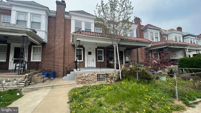 view of front of property with brick siding, a porch, and a chimney