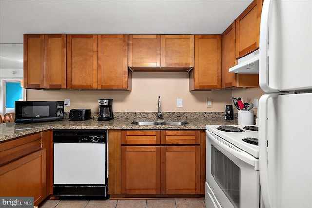 kitchen with a sink, under cabinet range hood, light tile patterned floors, brown cabinetry, and white appliances