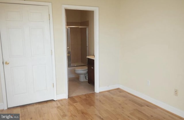 unfurnished bedroom with connected bathroom, baseboards, and light wood-type flooring