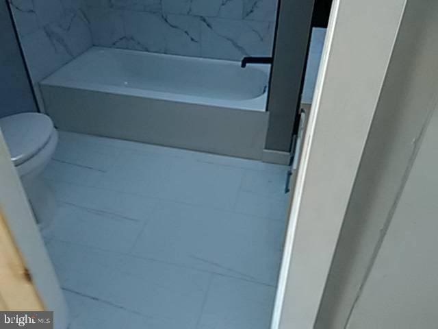 bathroom with tile patterned floors, a washtub, and toilet