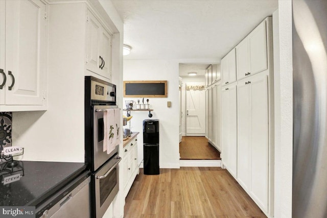kitchen featuring dark countertops, stainless steel dishwasher, white cabinetry, and light wood finished floors