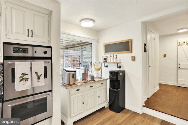 kitchen with light wood-type flooring, baseboards, white cabinets, and double oven