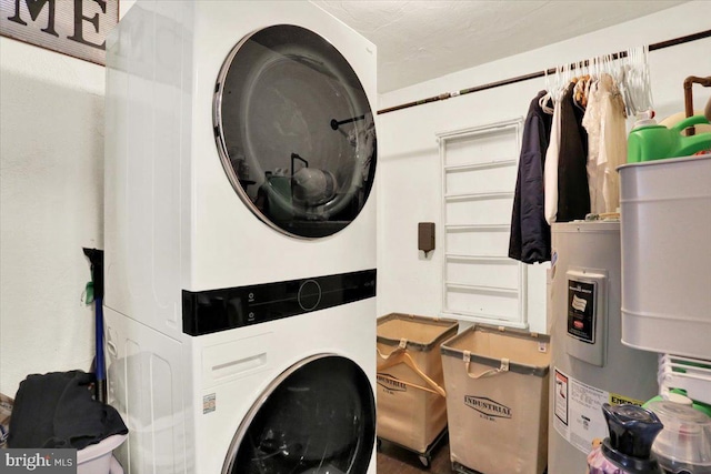 laundry room with electric water heater, stacked washing maching and dryer, and laundry area
