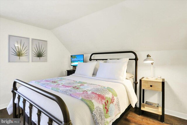 bedroom with baseboards, vaulted ceiling, and dark wood-type flooring
