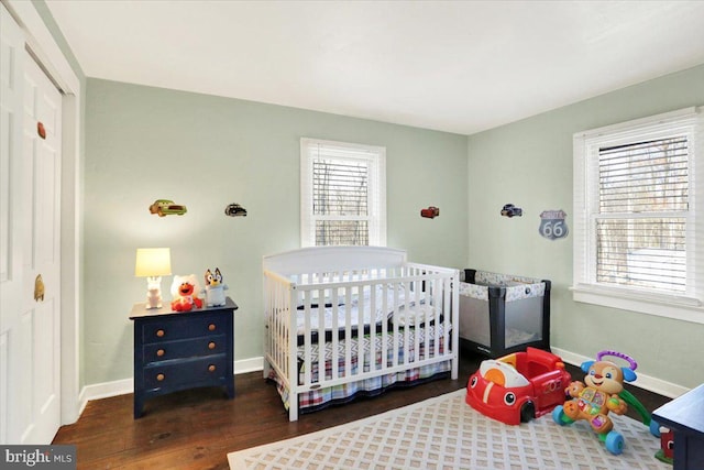 bedroom featuring baseboards, wood finished floors, a closet, and a nursery area