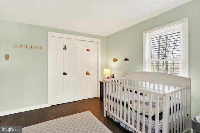 bedroom with hardwood / wood-style floors, a crib, baseboards, and a closet