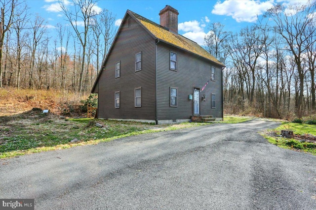 view of side of home with a chimney and aphalt driveway