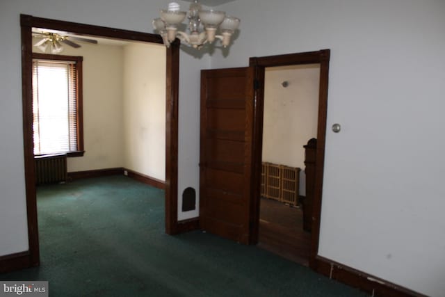 empty room featuring carpet floors, baseboards, ceiling fan with notable chandelier, and radiator heating unit