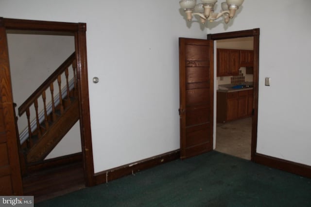 carpeted spare room featuring baseboards, a notable chandelier, and stairway