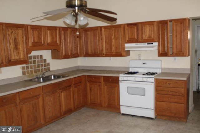 kitchen with ceiling fan, a sink, brown cabinetry, white gas stove, and under cabinet range hood