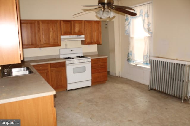 kitchen featuring a sink, ceiling fan, radiator heating unit, under cabinet range hood, and white gas range oven