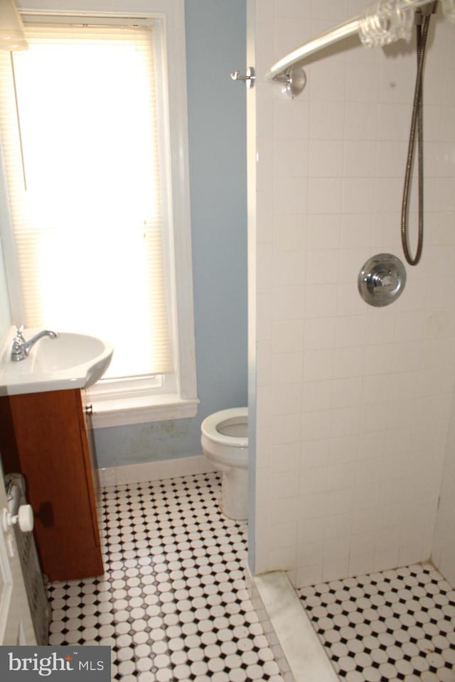 bathroom featuring toilet, tile patterned floors, a tile shower, and vanity