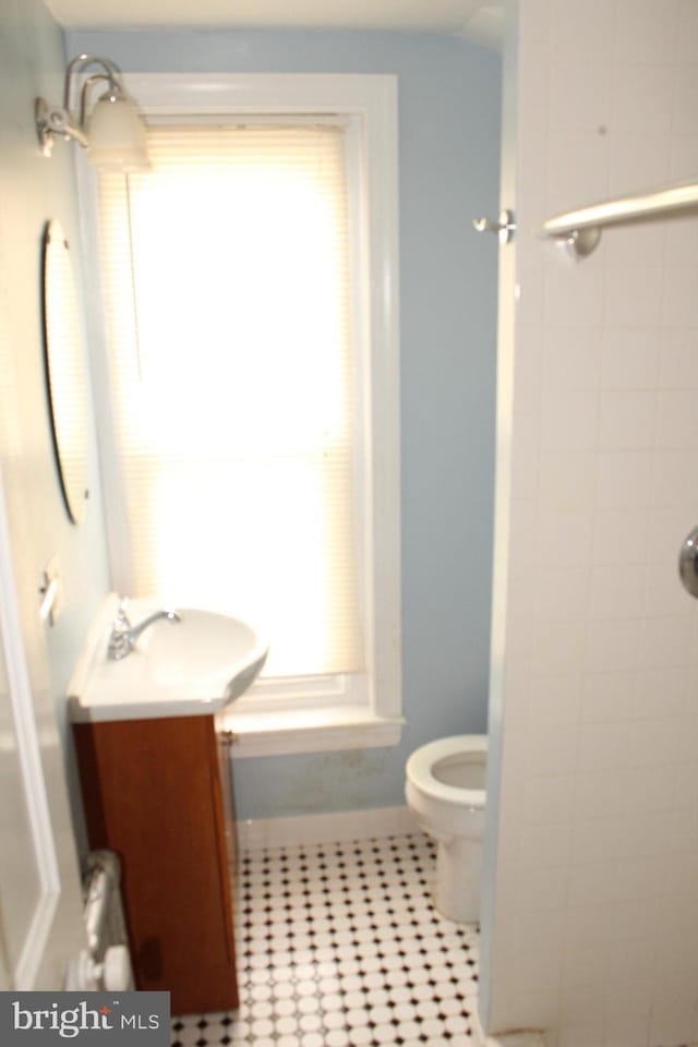bathroom featuring a healthy amount of sunlight, tile patterned flooring, vanity, toilet, and tiled shower