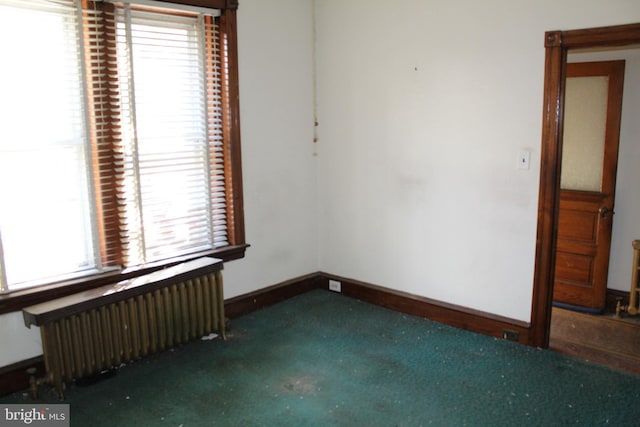 carpeted empty room featuring radiator and baseboards