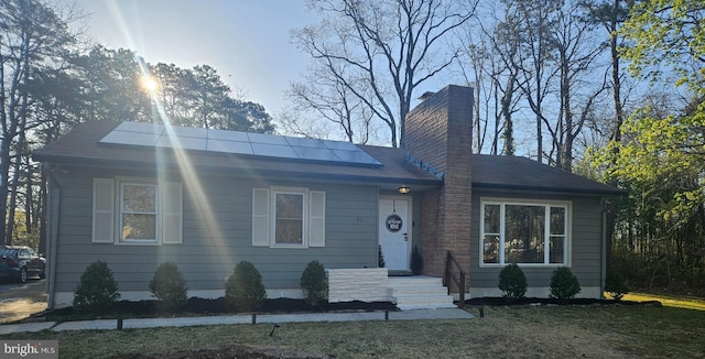 ranch-style home featuring roof mounted solar panels, roof with shingles, and a chimney