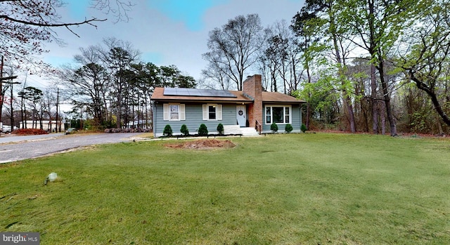 view of front facade with roof mounted solar panels, a chimney, a front yard, and aphalt driveway