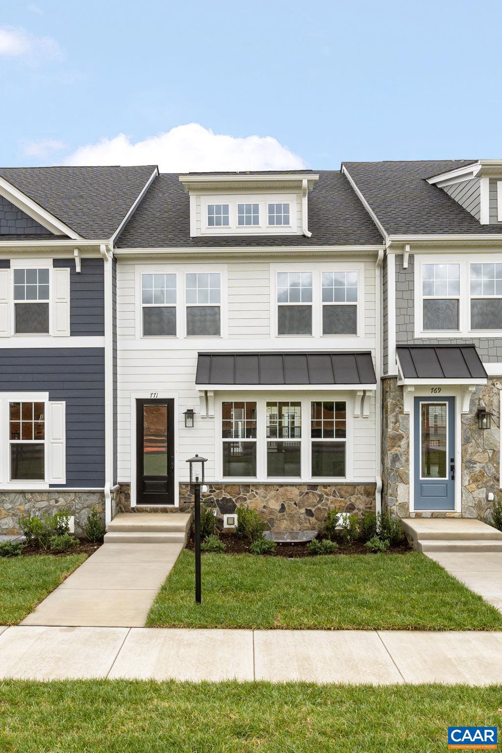 townhome / multi-family property with stone siding, a front yard, and a shingled roof
