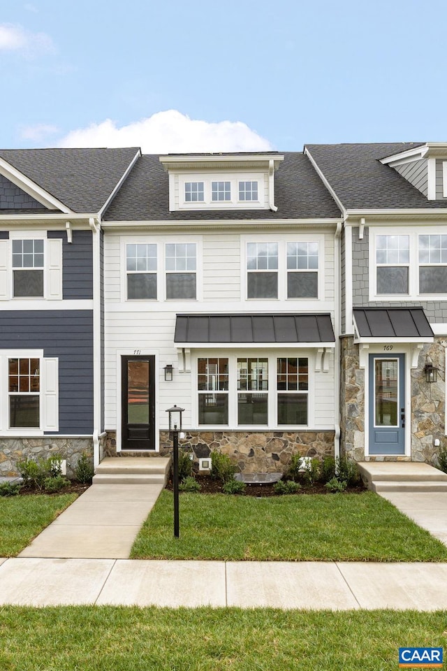townhome / multi-family property with stone siding, a front yard, and a shingled roof