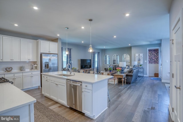 kitchen with light countertops, a sink, hanging light fixtures, appliances with stainless steel finishes, and open floor plan