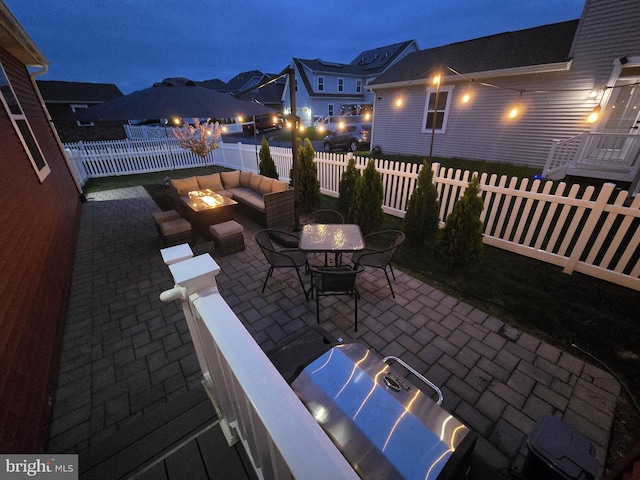 patio at night with a fenced backyard and an outdoor living space with a fire pit