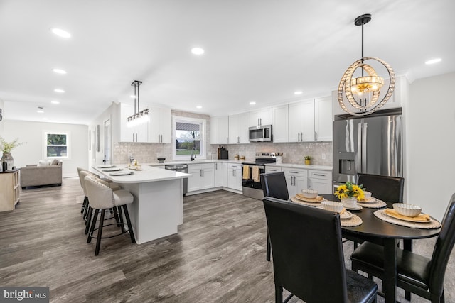 kitchen with white cabinets, an inviting chandelier, backsplash, a peninsula, and appliances with stainless steel finishes