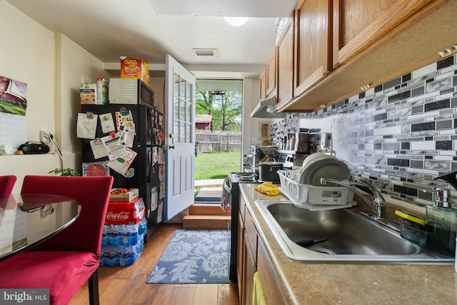 kitchen with a sink, tasteful backsplash, visible vents, wood finished floors, and brown cabinets