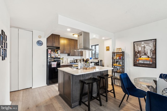 kitchen with freestanding refrigerator, a kitchen breakfast bar, light countertops, island exhaust hood, and light wood-style flooring