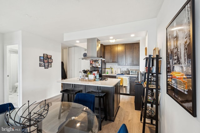 kitchen with island exhaust hood, tasteful backsplash, dishwasher, light countertops, and light wood-style floors