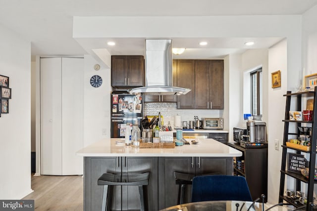 kitchen with light wood-style floors, light countertops, freestanding refrigerator, island range hood, and tasteful backsplash