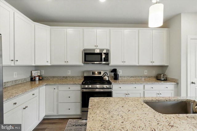 kitchen featuring white cabinets, dark wood finished floors, stainless steel appliances, a sink, and light stone countertops