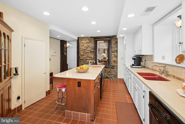 kitchen featuring a kitchen breakfast bar, a sink, an island with sink, light countertops, and visible vents