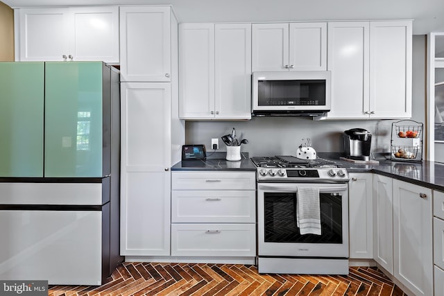 kitchen with freestanding refrigerator, white cabinetry, dark countertops, and gas range