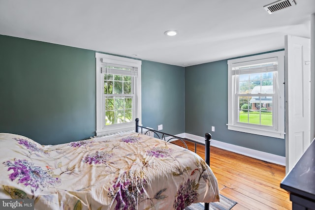 bedroom with visible vents, baseboards, multiple windows, and hardwood / wood-style floors