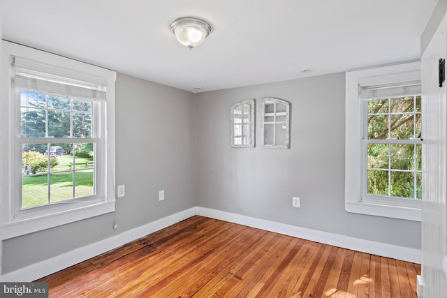 spare room featuring baseboards, a wealth of natural light, and hardwood / wood-style floors