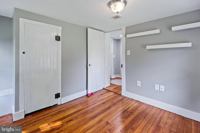 unfurnished bedroom with wood-type flooring, baseboards, visible vents, and a closet