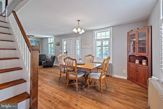 dining space featuring an inviting chandelier, light wood-style flooring, radiator, stairs, and baseboards