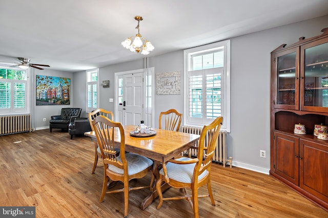 dining room with light wood-style floors, radiator, ceiling fan with notable chandelier, and baseboards