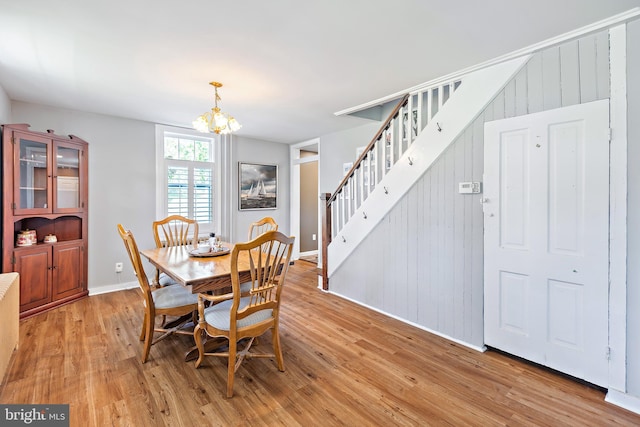 dining space with wood walls, baseboards, stairway, light wood-style flooring, and a notable chandelier
