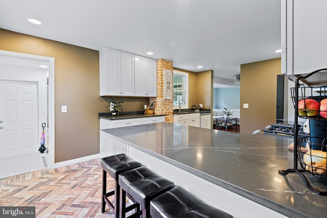 kitchen with dark countertops, a sink, brick floor, a breakfast bar area, and white cabinetry